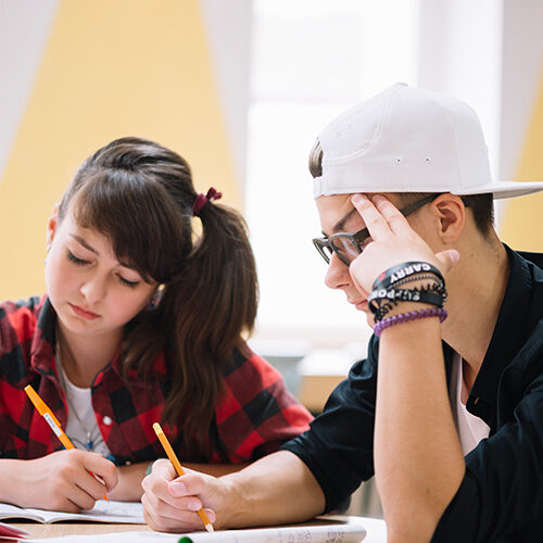 Two students studying together at a desk, writing notes and working on assignments.